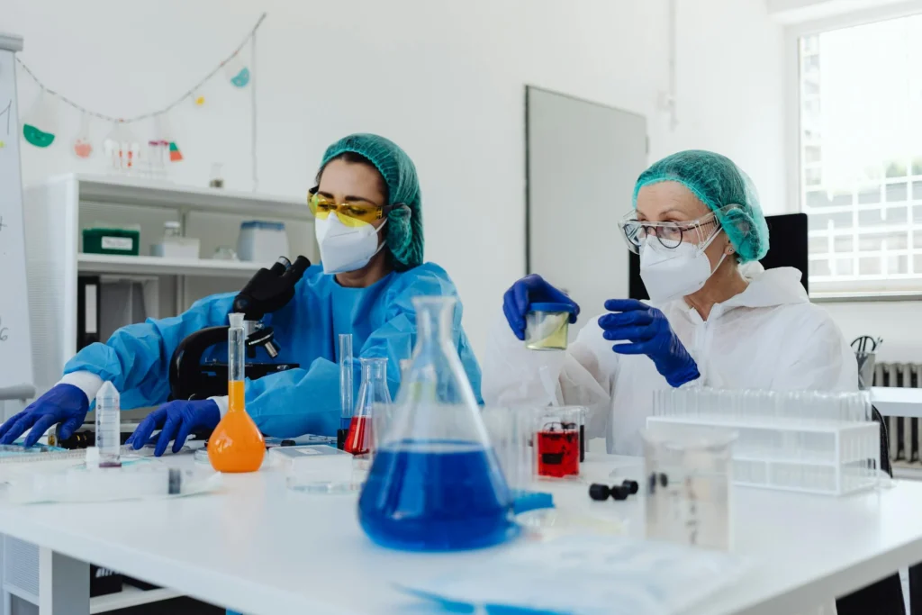 Two scientists in protective lab gear conducting chemical analysis and formulation research with colorful reagents and lab equipment in a modern laboratory.